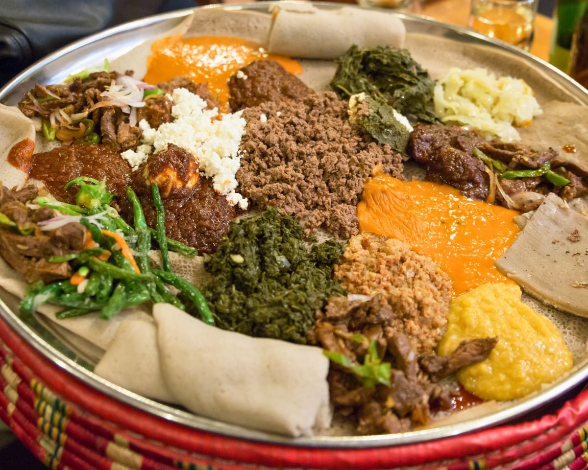 A shared injera platter: wot, greens and ayib in a mesob